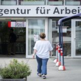 لقطة خارجية لمدخل وكالة العمل الألمانية "Agentur für Arbeit" تظهر امرأة تسير نحو الأبواب الزجاجية للمبنى تحت لافتة الشركة الرسمية.