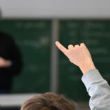 لقطة مقربة من الخلف لطلاب مراهقين يجلسون على مقاعدهم داخل صف مدرسي حديث في ألمانيا، يركزون في دفاترهم أثناء الحصة الدراسية.