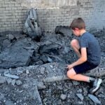 Ein Kind betrachtet ein zerstörtes Gebäude in Kyjiw.