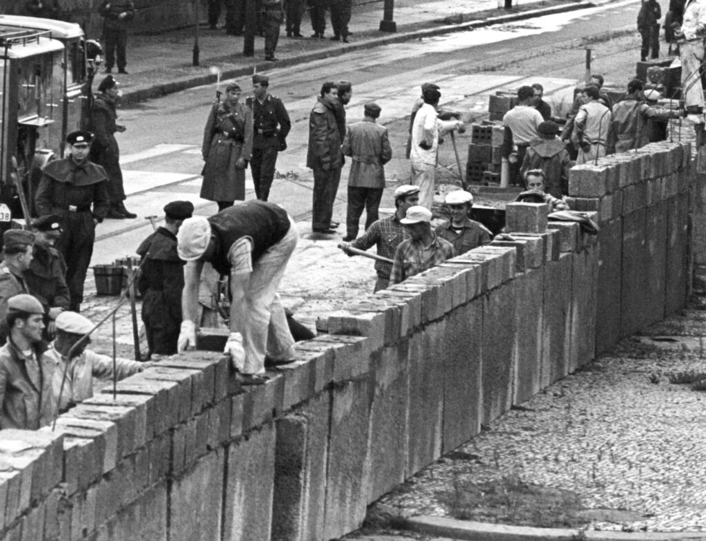 آرشیو - ۱۸ آگوست ۱۹۶۱، جمهوری دموکراتیک آلمان، برلین: تیمی از آجرچین‌های برلین شرقی، تحت نظارت افسران مسلح پلیس مردمی، دیواری را در مرز بخش شوروی-آمریکا در میدان پوتسدامر برپا می‌کنند. 
Foto: UPI/dpa