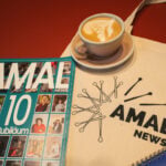 Das Bild zeigt einen Stoffbeutel, auf dem „Amal News“ steht. Darauf liegen ein Printmagazin mit dem Titel „AMAL 10“. Daneben steht eine Tasse mit Kaffee.