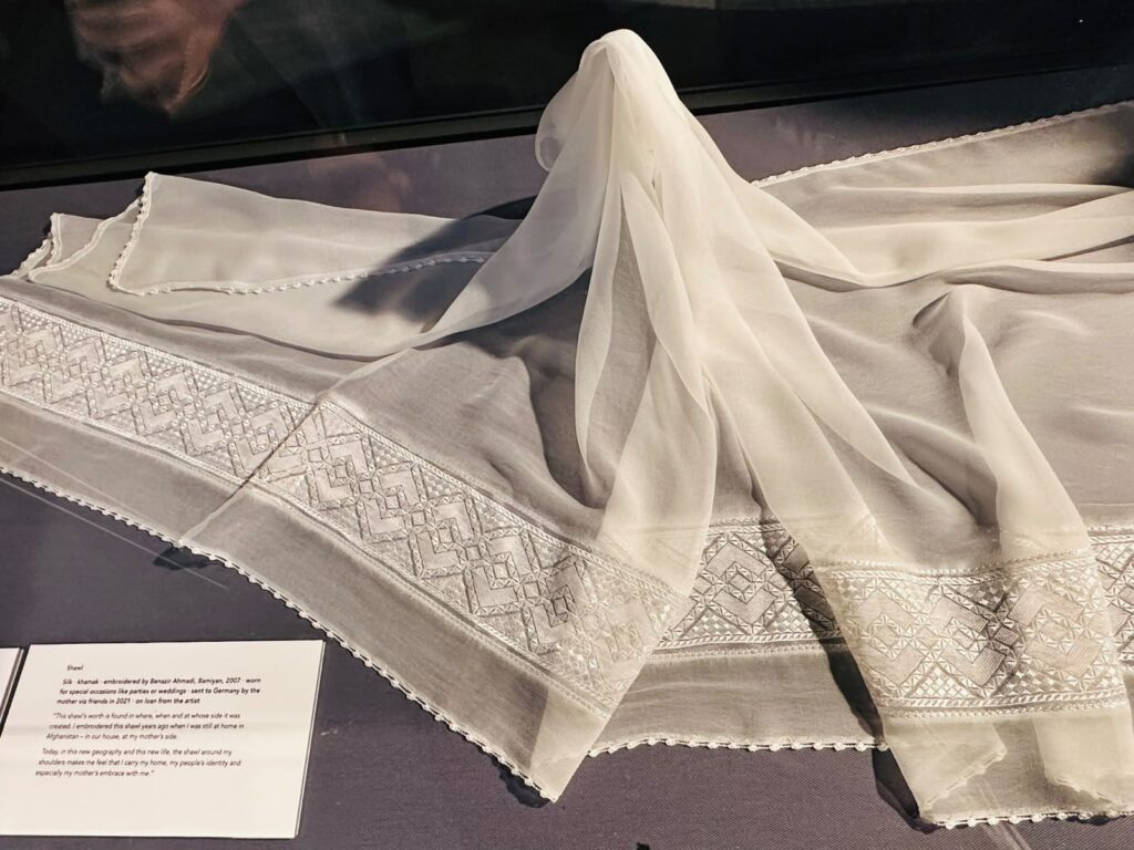 Das Foto zeigt ein weißes besticktes Tuch in einer Vitrine.